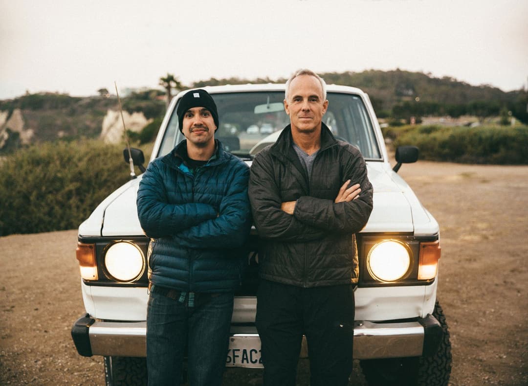 Two men standing next to each other in front of a car