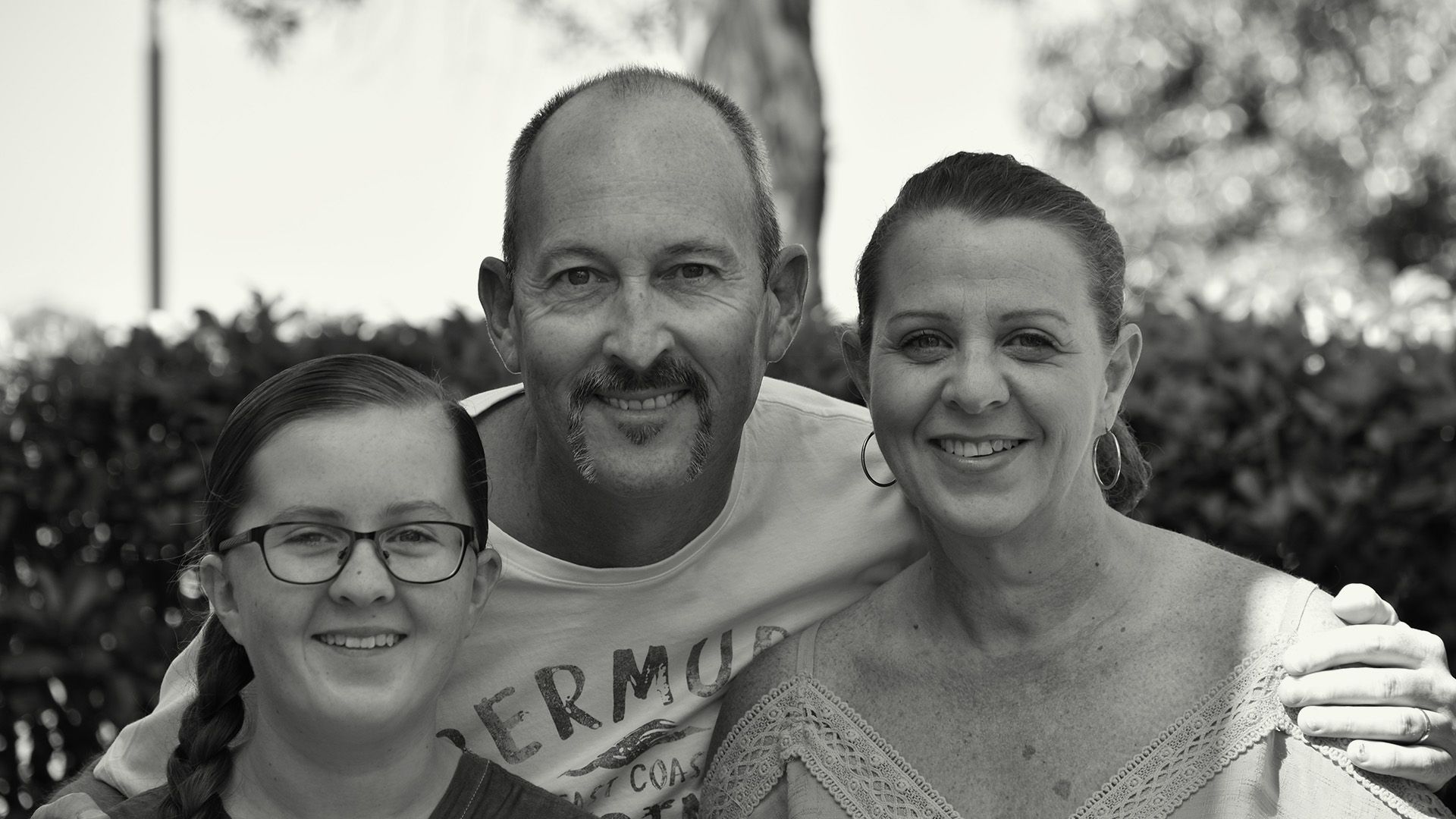 Black and white photo of family, left is young daughter with glasses, right is mother, and behind in the middle is father