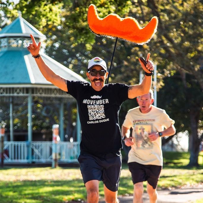 Photo of an exuberant man, running toward camera. A bright, floating Movember moustache logo is suspended behind him.