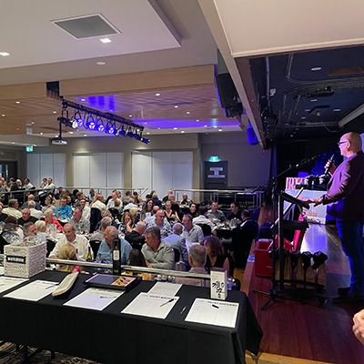 A busy evening in the games room at an RSL Club, showing an MC addressing a rowdy crowd.
