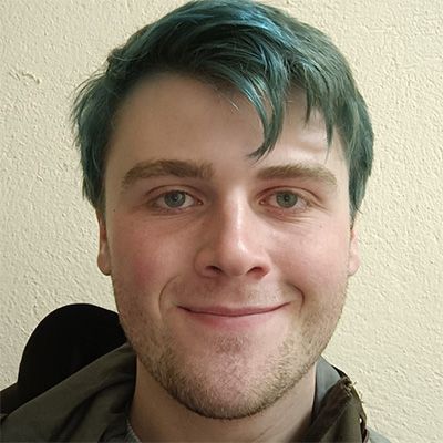Young man with dyed green hair smiling to camera.