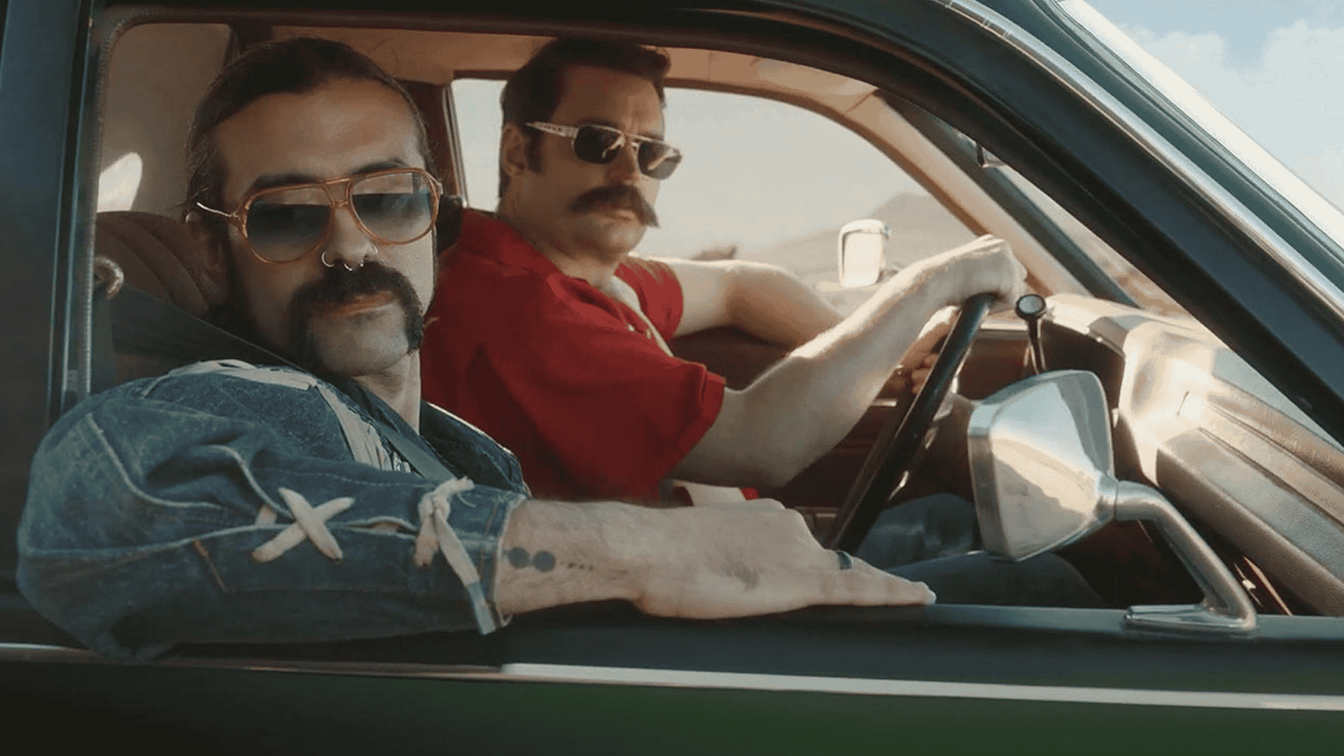 Photo of two cool-looking dudes with splendid moustaches, looking to camera from a car.