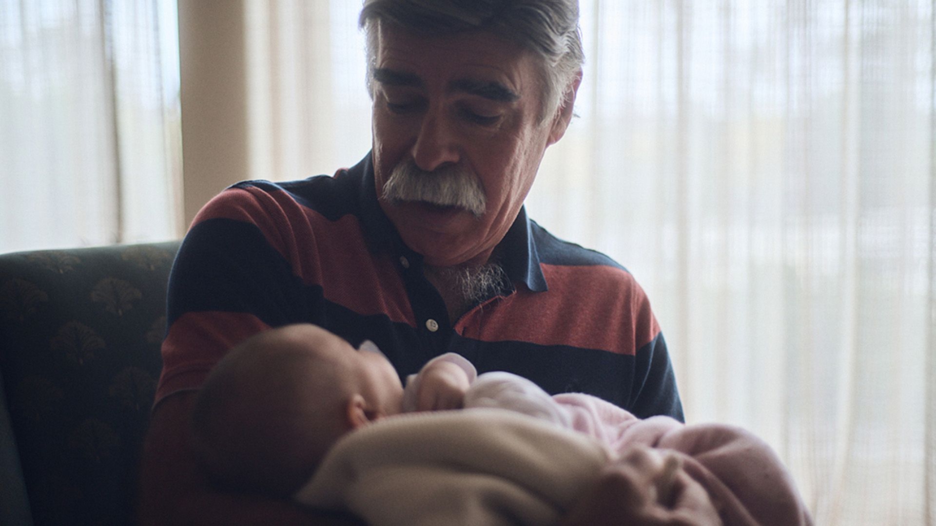 Photo of a sitting grandfather lovingly cradling an infant grandchild.