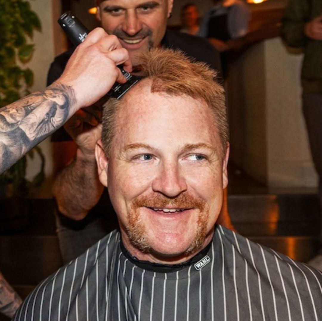 Portrait photo of a man having his head shaved in a barber chair.