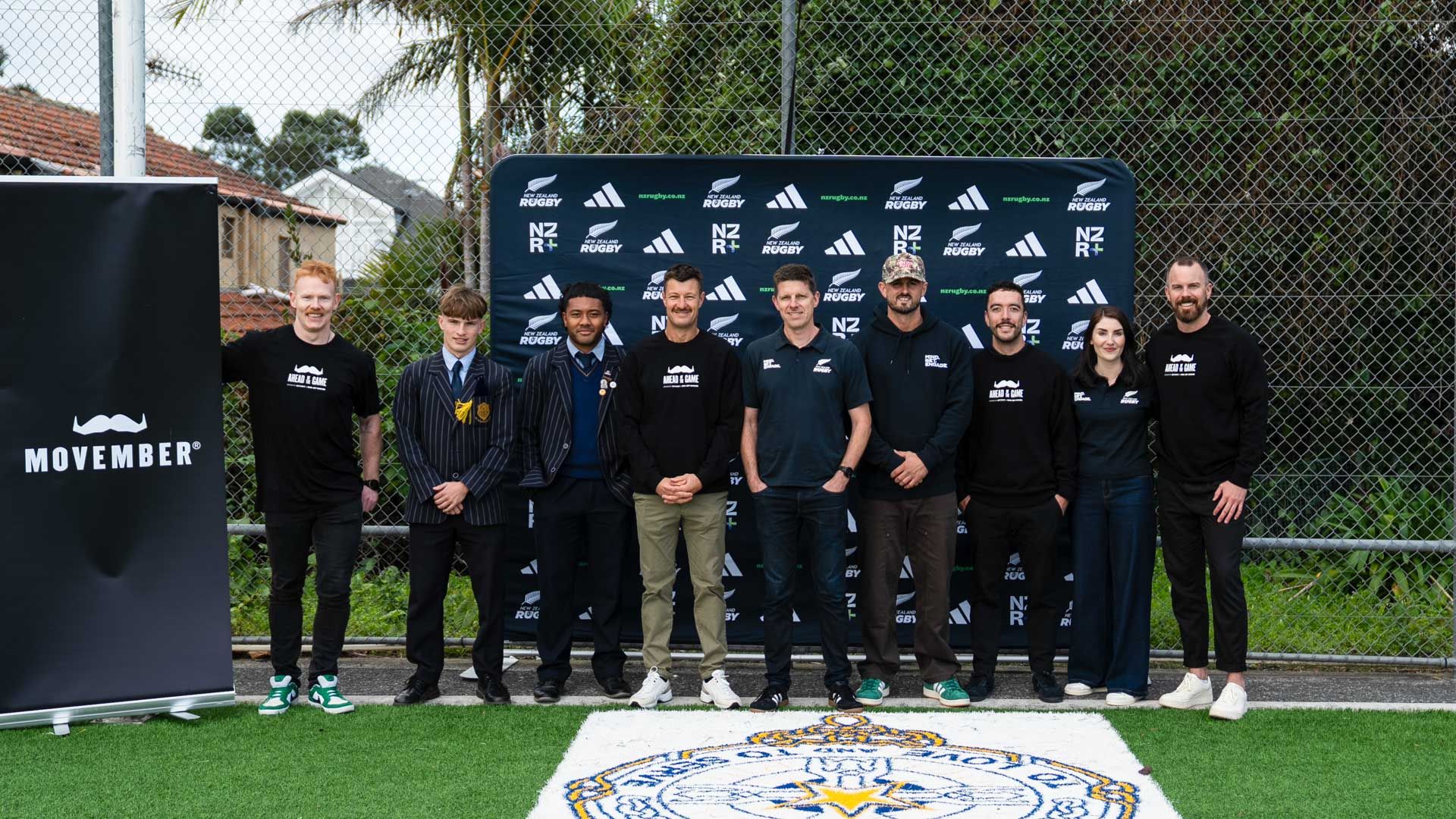 Group of people stand in front of media wall on rugby field for launch event of sports programme