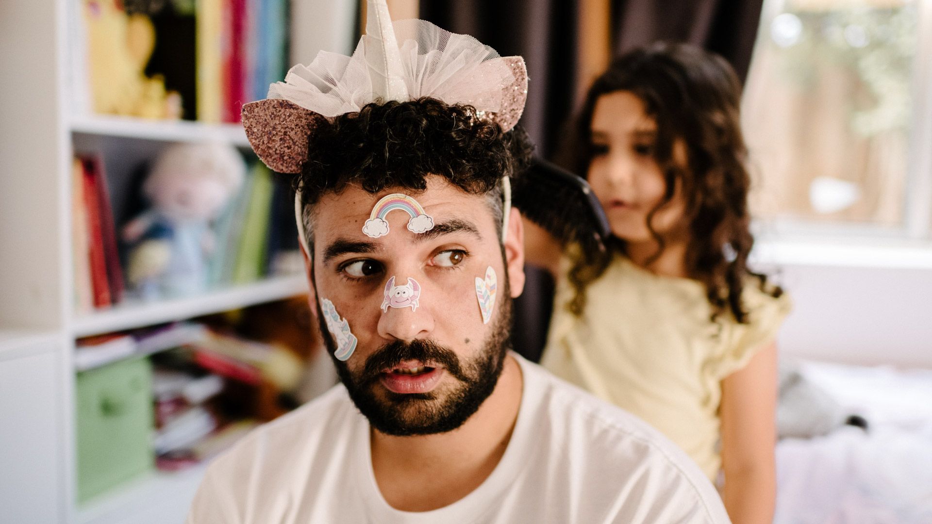 Dad with face paint and tiara with young daugther behind dressing up dad