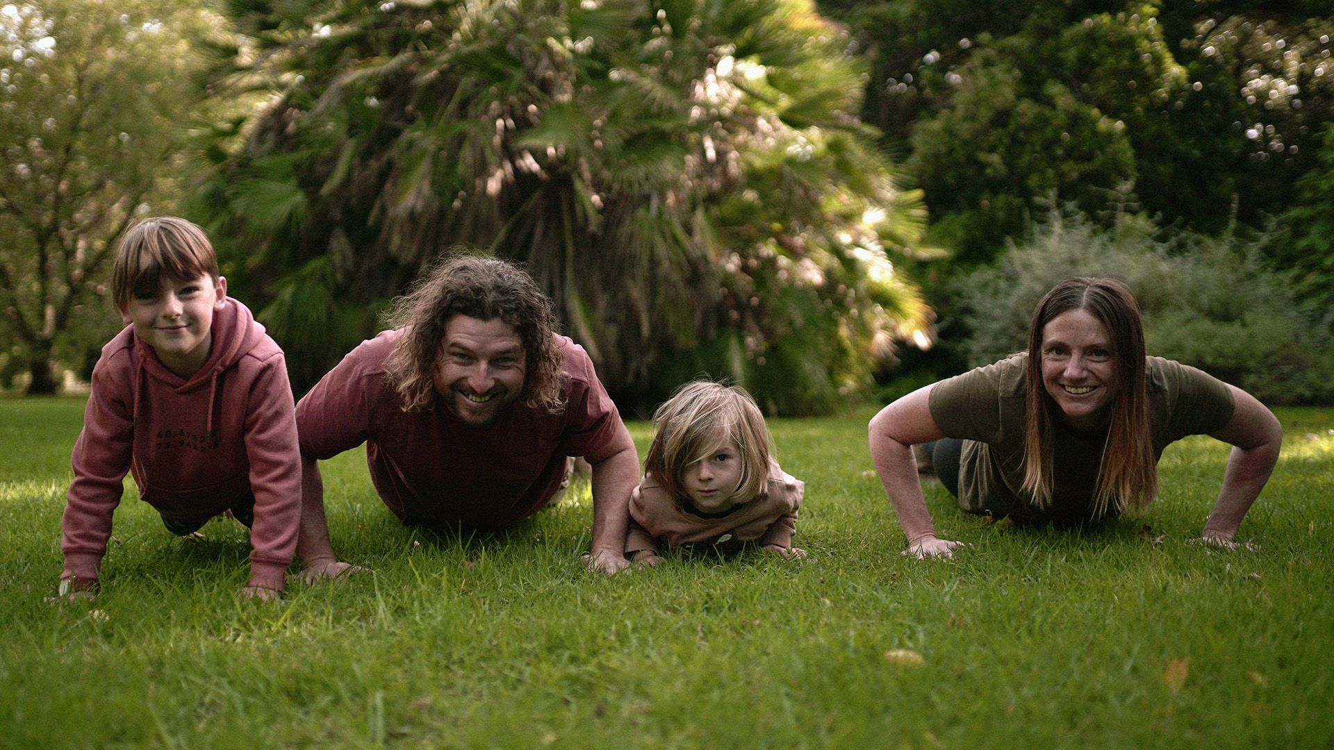 The Bailey family pushing up together on grass in a park.