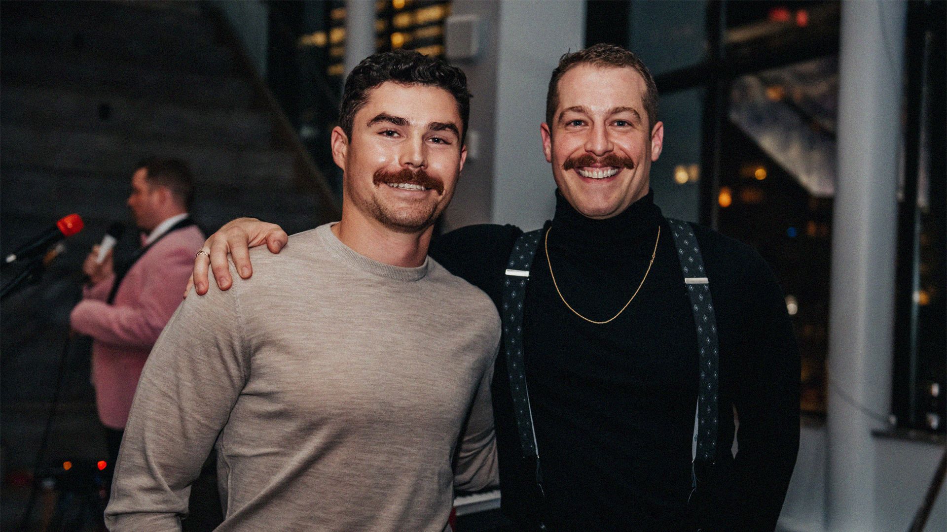 Photo of two men, donning superb moustaches, smiling to camera.