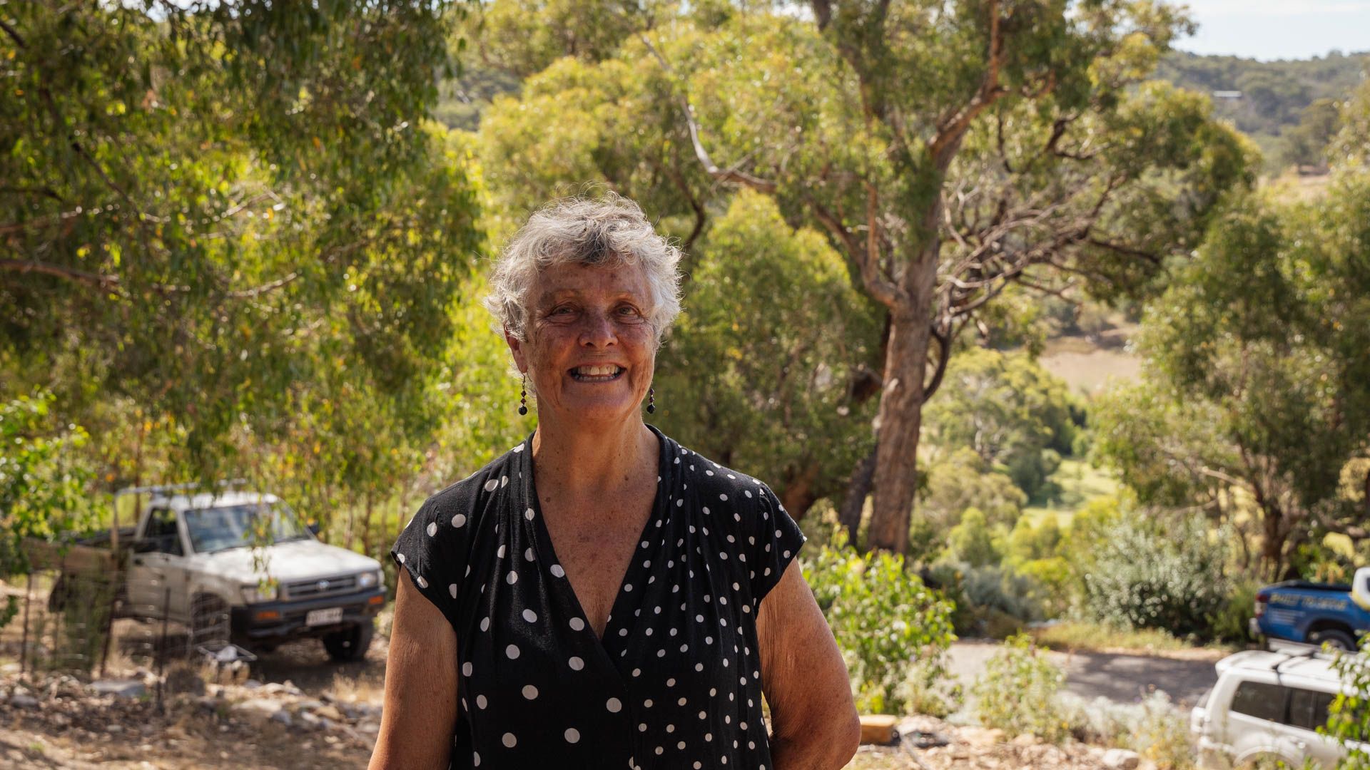 Woman stands smiling at camera with bush and trees behind and a white ute