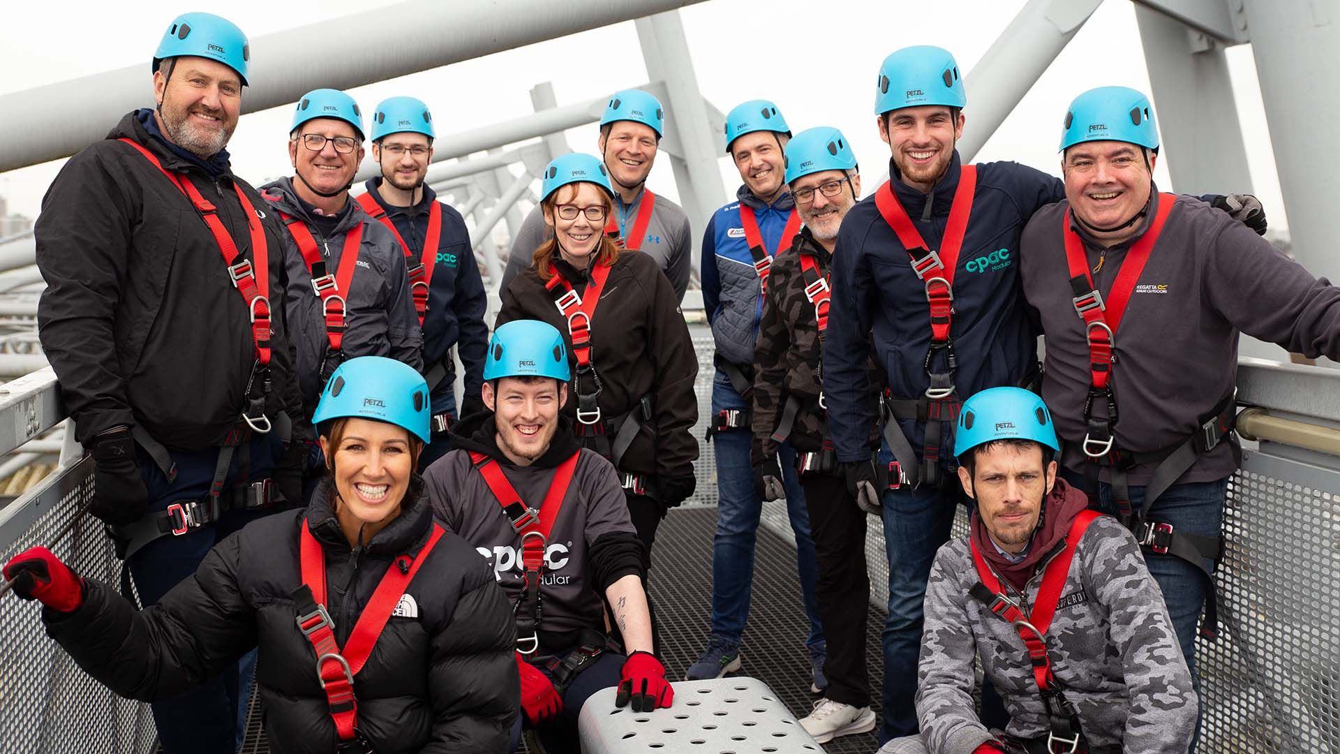 Photo of an office team dressed in safety gear, about to abseil a bridge.