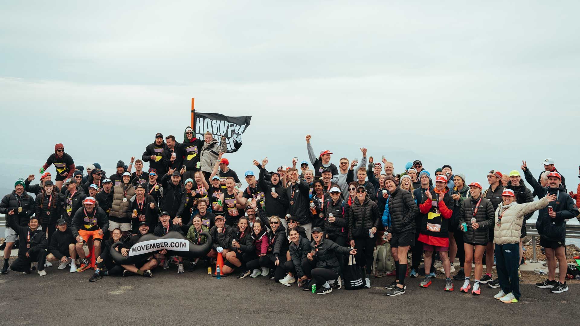 Photo of marathon spectators on a mountain, holding up Movember signage.