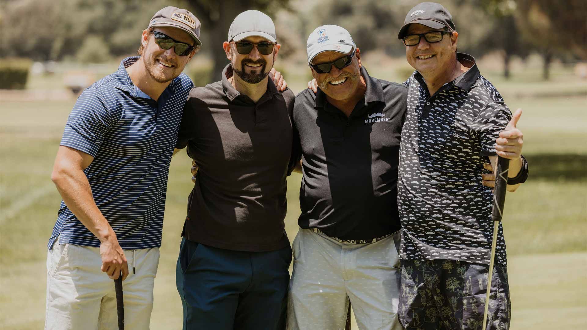 Photo of four men smiling to camera, dressed in golfing attire and ready to tee off.