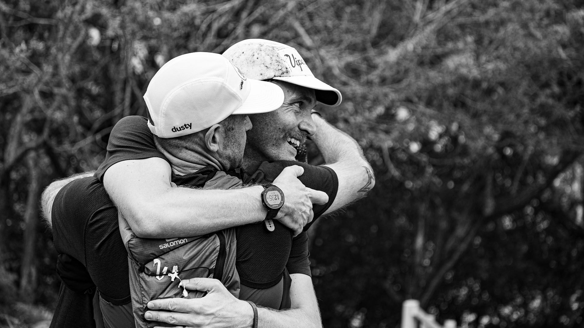 Black and white photo of two men in running gear, embracing after raising funds for Movember.