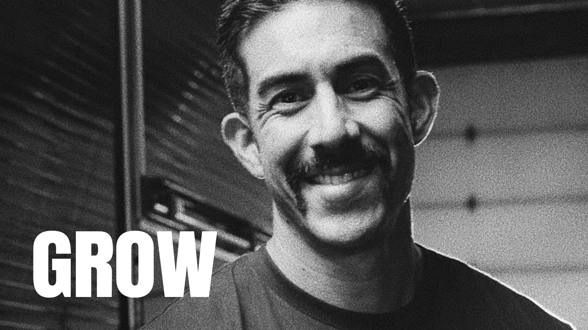 A black and white photo of a man smiling to camera. The word "GROW" is superimposed.