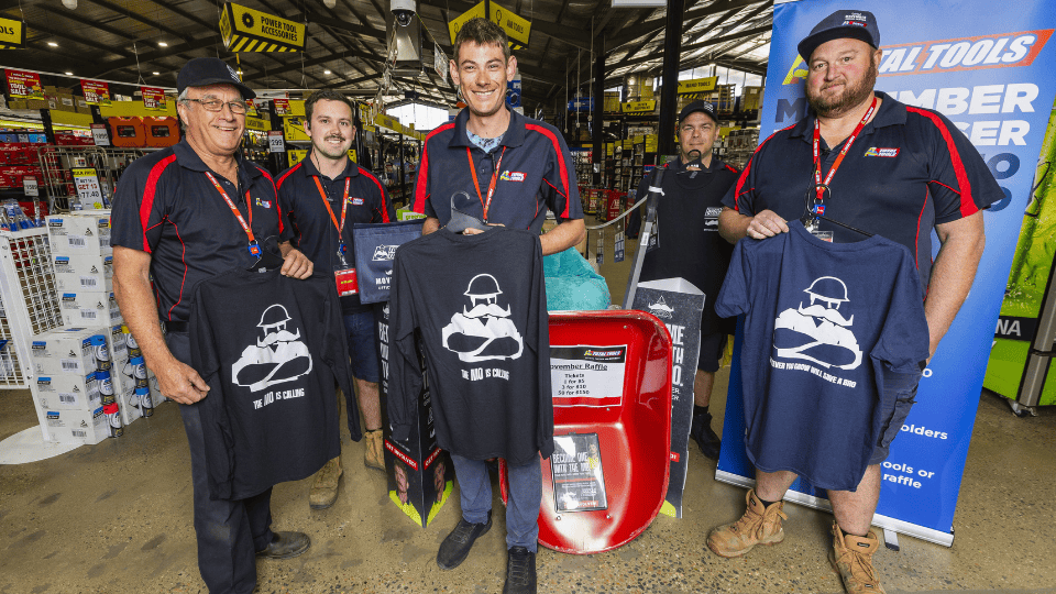 An image of five staff standing within a Total Tools store holding up Movember x Total Tools merchandise.