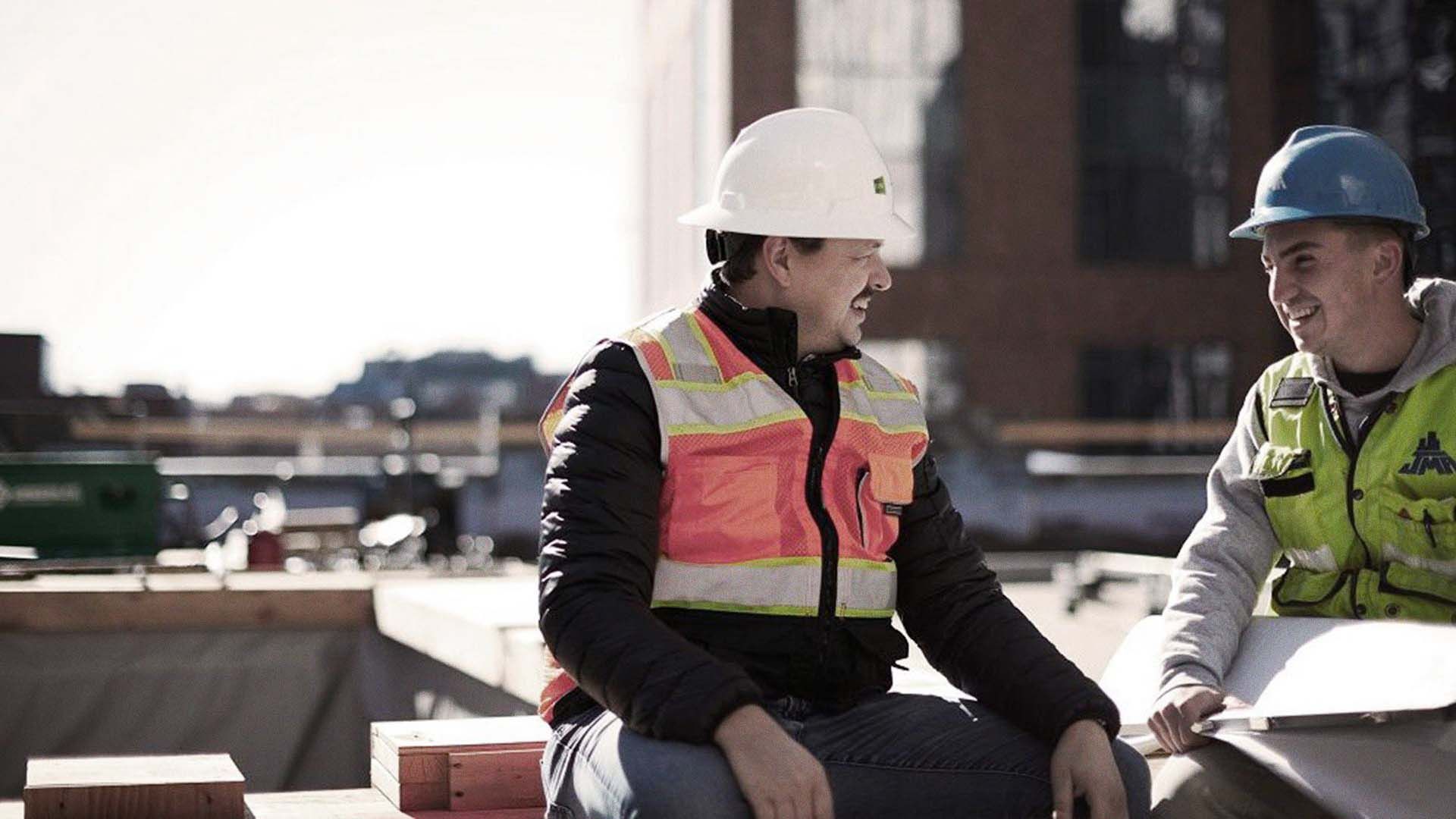 Photo of two construction workers on a building site, wearing high-visibility gear and protection.