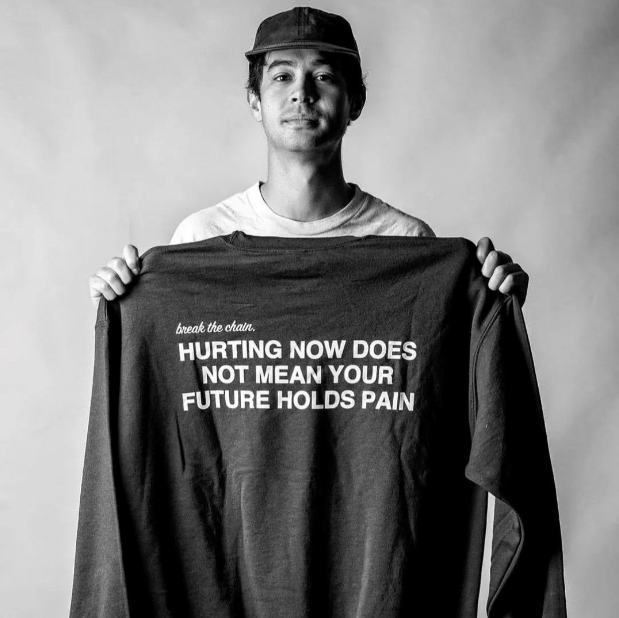 Man looking to camera, holding up a long-sleeve shirt. It says: "Hurting now does not mean your future holds pain."