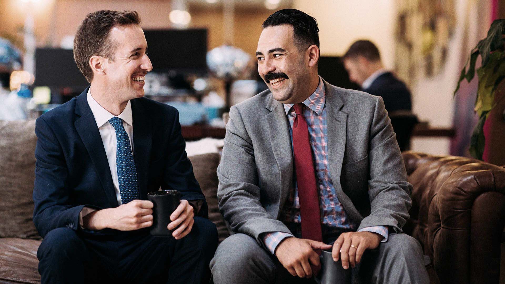 Photo of two suited dapper-looking men in suits. Both have excellent moustaches.